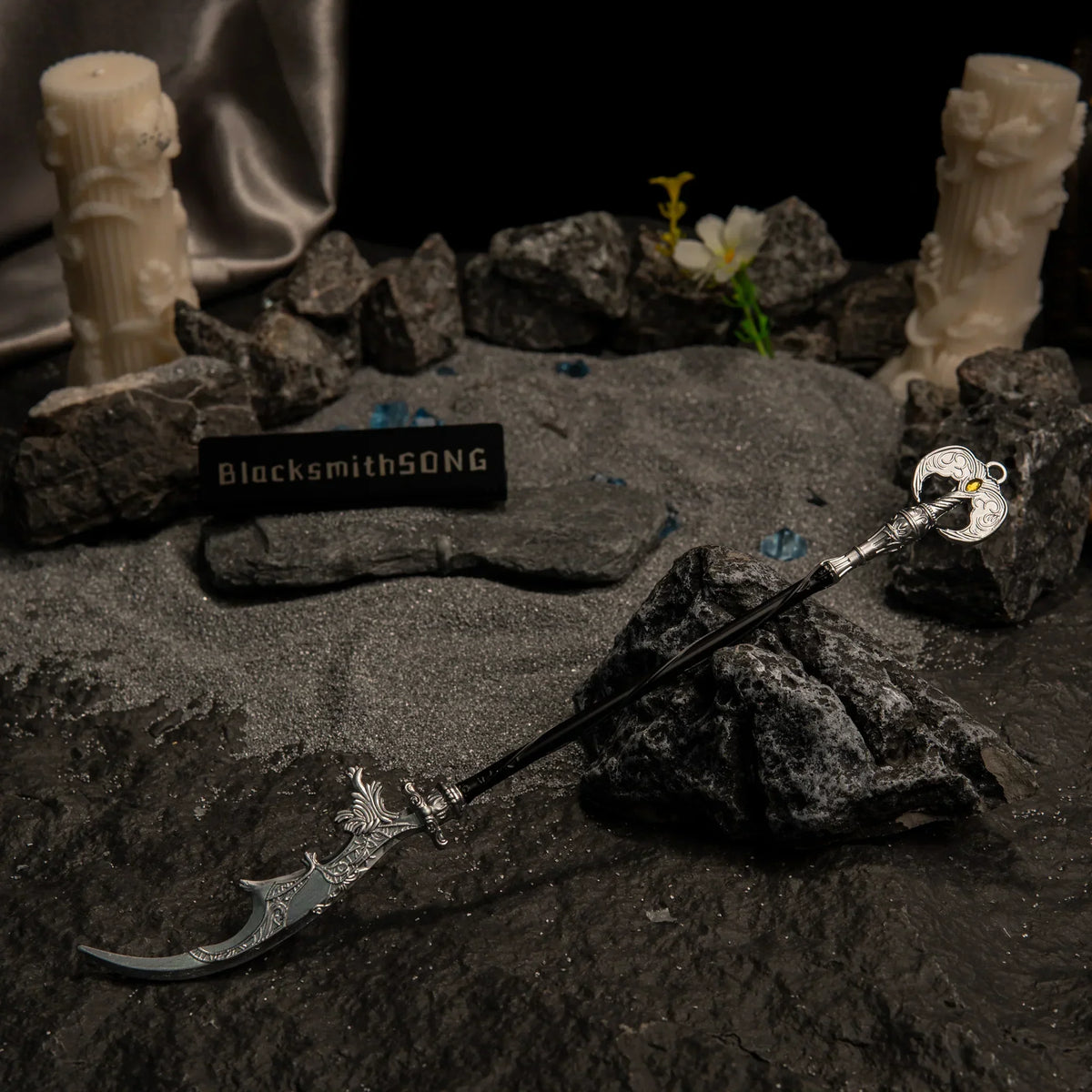 Loretta's War Sickle metal replica resting on dark rocks and grey sand, surrounded by white carved pillar candles, blue glintstone shards, and a white flower.
