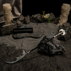Loretta's War Sickle metal replica resting on dark rocks and grey sand, surrounded by white carved pillar candles, blue glintstone shards, and a white flower.