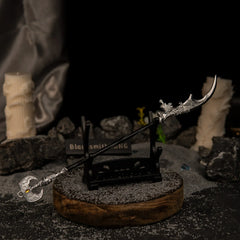 Loretta's War Sickle miniature resting horizontally on a small black stand, positioned diagonally across a wooden base with a lit candle background.