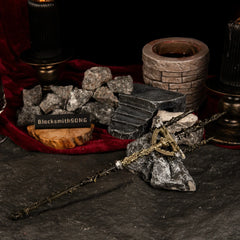 Side-profile of the Mohgwyn's Sacred Spear metal miniature leaning against a jagged dark rock with a BlacksmithSONG logo sign and ritualistic props.