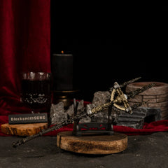 Mohgwyn's Sacred Spear miniature weapon placed on a small horizontal wooden stand with blurred black candles and red velvet in the background.