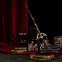 Vertical display of the Mohgwyn's Sacred Spear replica on an upright stand, positioned like a ritual staff next to a black candle and stone ruins.