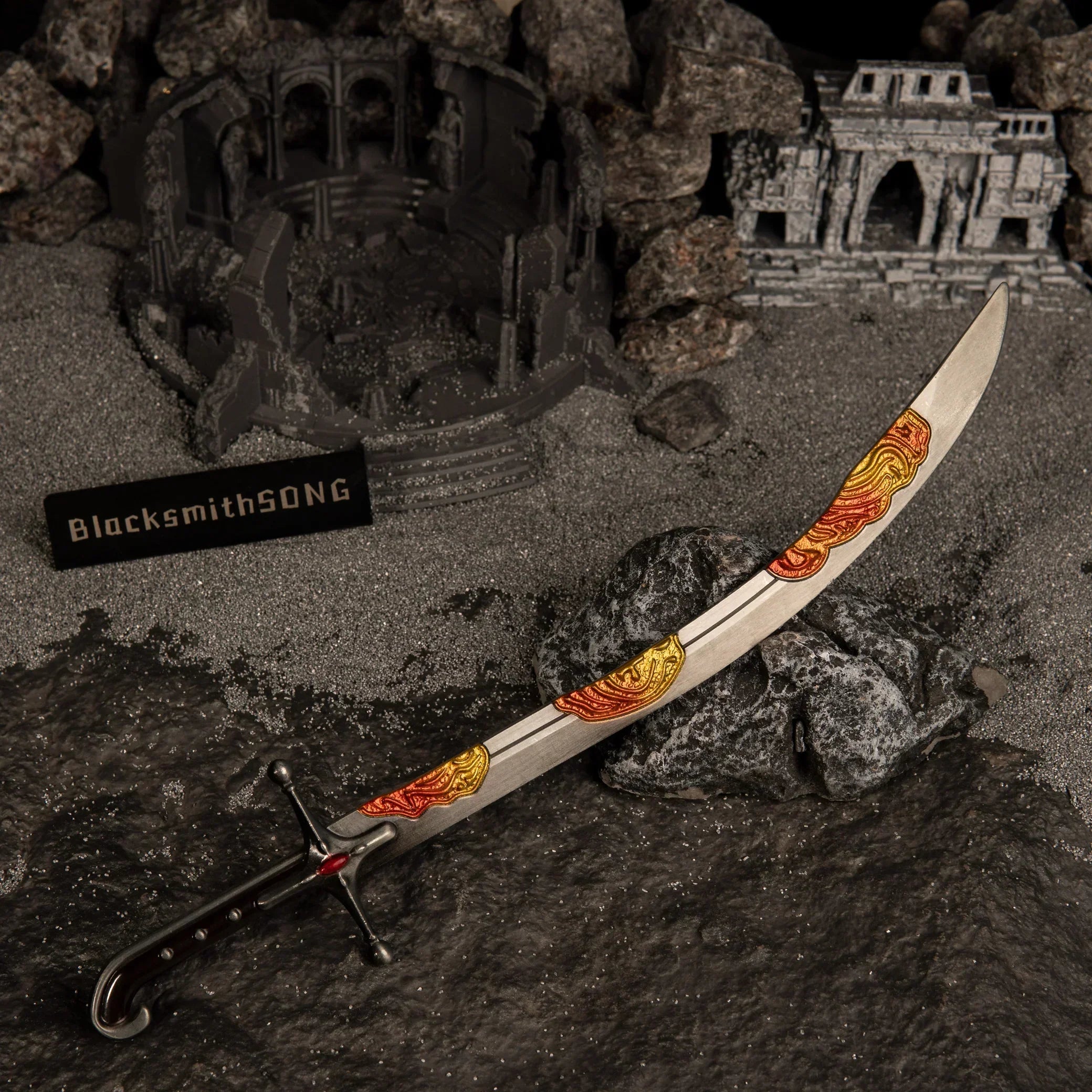 Nomad's Kilij curved sword metal replica resting on a dark rock, surrounded by grey ash-like sand and a miniature ruined colosseum diorama.