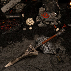 Serpent-Hunter metal replica resting on a dark volcanic rock, surrounded by black sand and miniature human skulls.