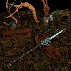 Spear of the Dreaming metal replica resting diagonally on dark driftwood, surrounded by green moss, scattered blue crystals, and miniature rune stones.
