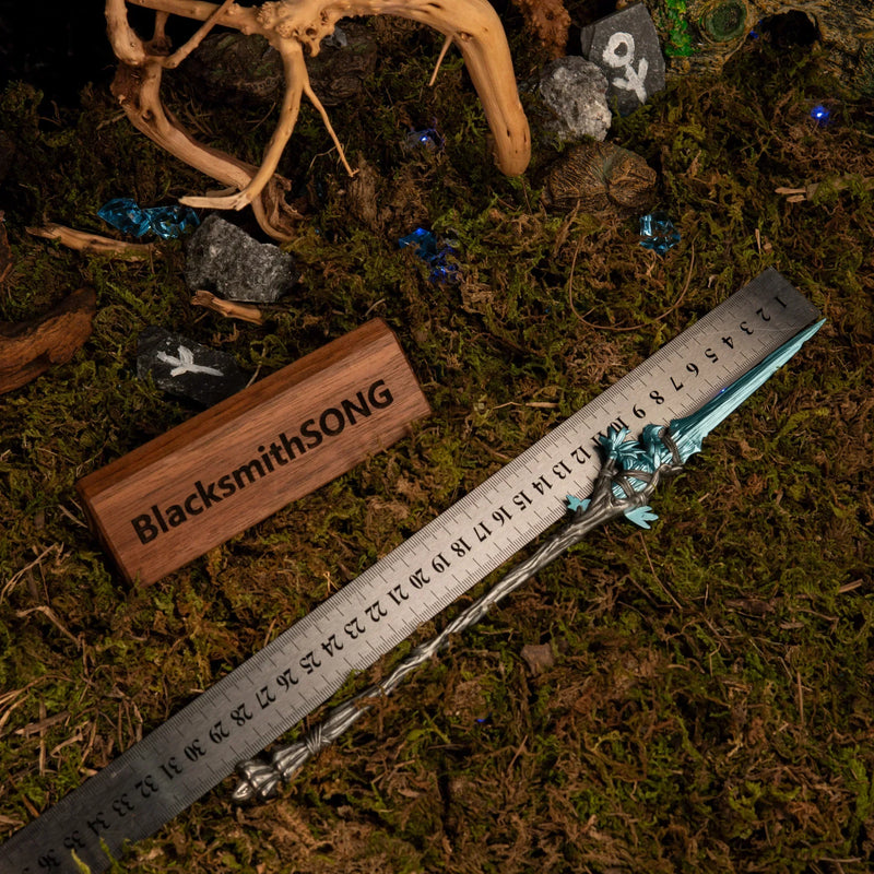 Spear of the Dreaming metal replica placed next to a measuring ruler on green moss, indicating a total length of approximately 30 centimeters.
