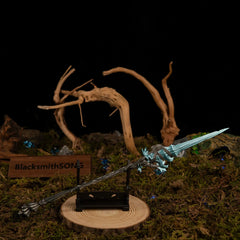 Spear of the Dreaming miniature resting horizontally on a small black stand, positioned on a wooden base surrounded by twisted driftwood and moss.