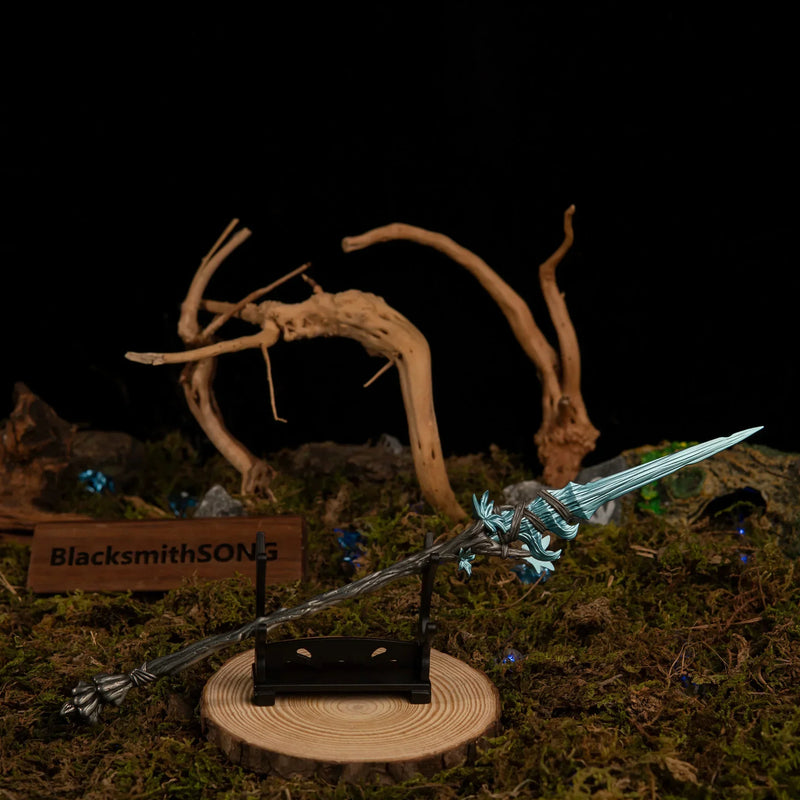 Spear of the Dreaming miniature resting horizontally on a small black stand, positioned on a wooden base surrounded by twisted driftwood and moss.