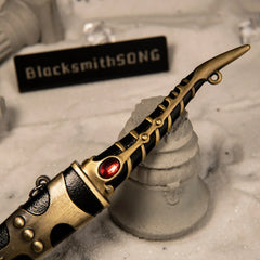 Catspaw Dagger replica — hooked crossguard and red faceted inset, close-up on rock.
