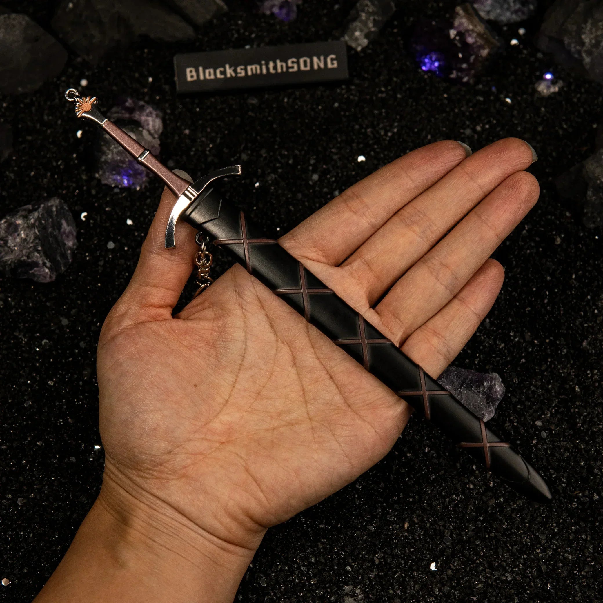 Hand holding the 22cm Dawn metal replica sword and its black scabbard to show scale.