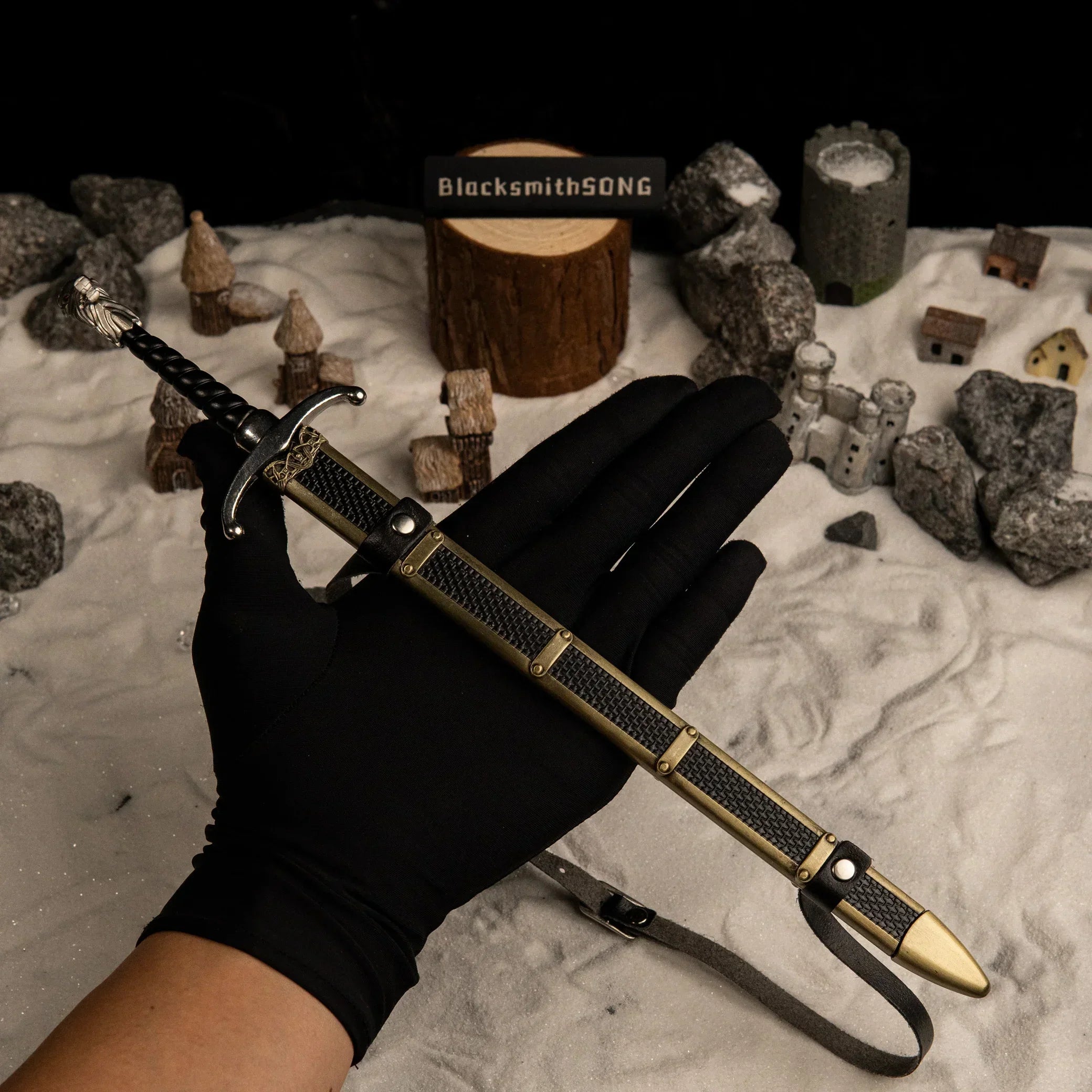 A hand wearing a black glove holding the 30cm Longclaw metal replica and its detailed scabbard to show its scale, set against a snowy background.