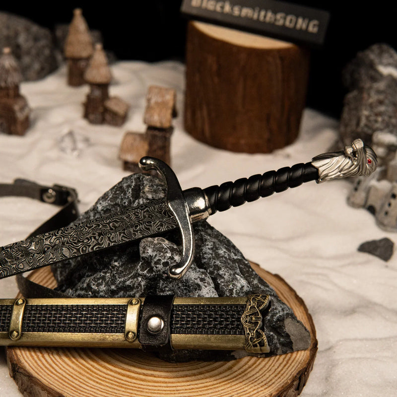 Longclaw replica — hilt, crossguard and wolf's-head pommel against snow-set rocks.
