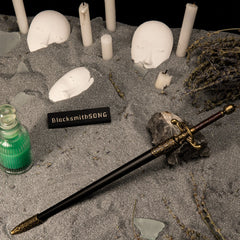 Needle replica — sheathed in its black-and-gold scabbard among pale candles and masks.
