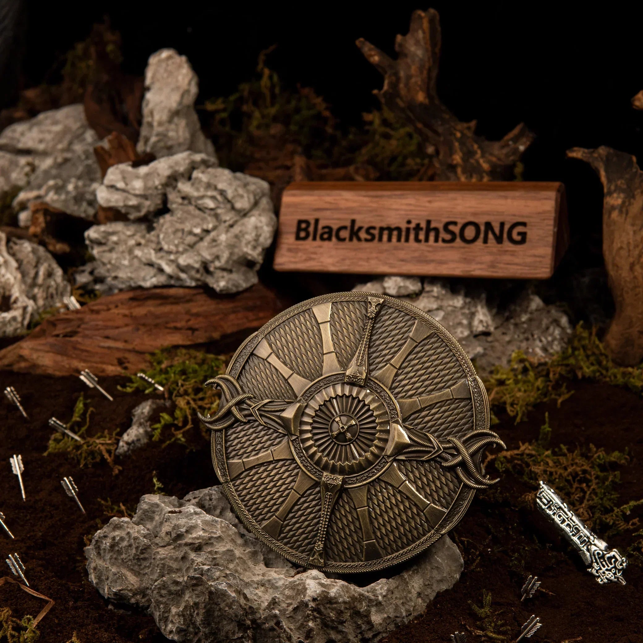 A circular 10cm bronze metal Guardian Shield replica resting on a grey rock in a dark moss and soil diorama with miniature arrows stuck in the ground.