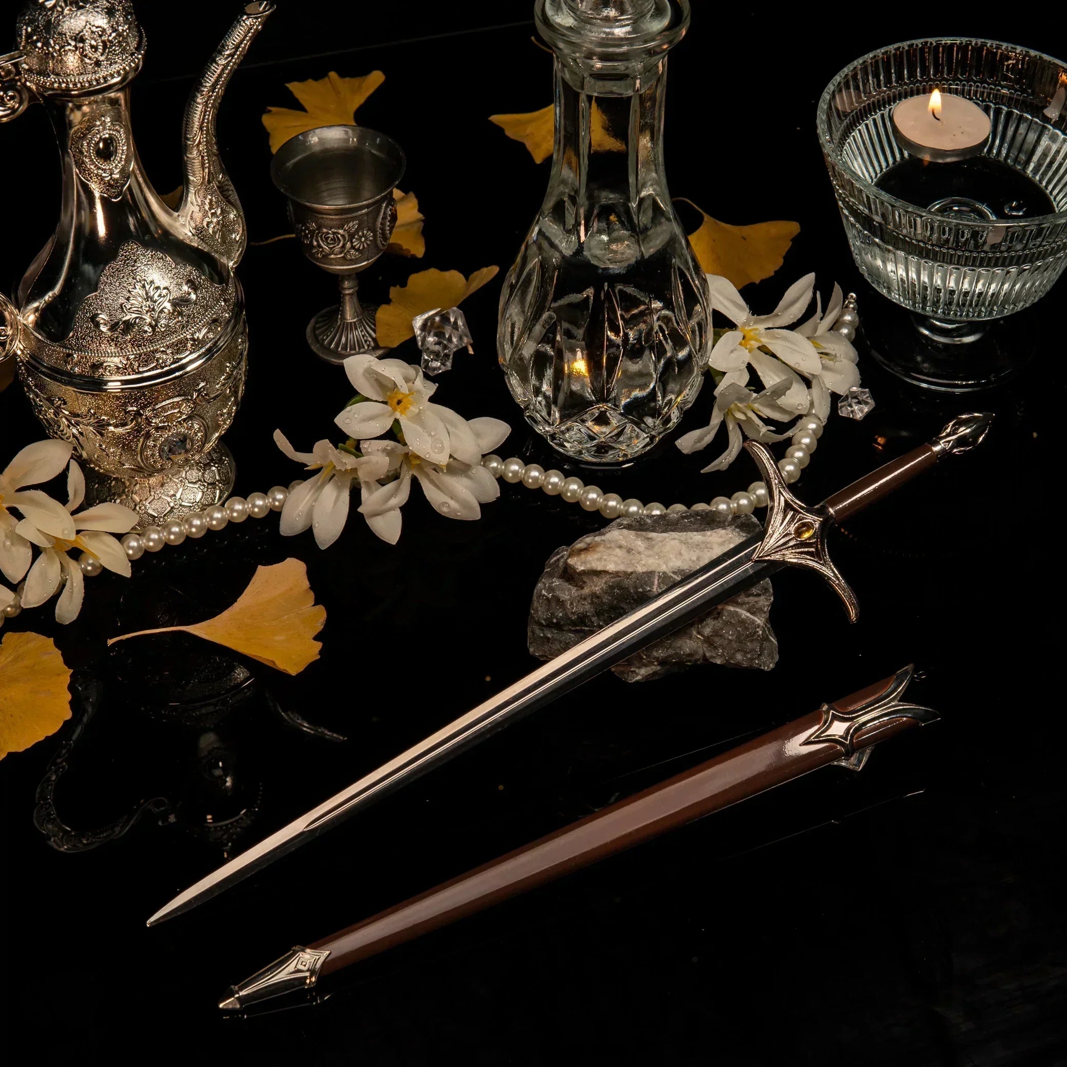 Galadriel metal sword replica unsheathed on a black reflective surface, surrounded by silver vintage teaware, pearls, and yellow ginkgo leaves.