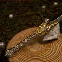 Galadriel's Dagger replica — gold-wrapped hilt flowing into the silver blade, on a wood slice with a small stone.