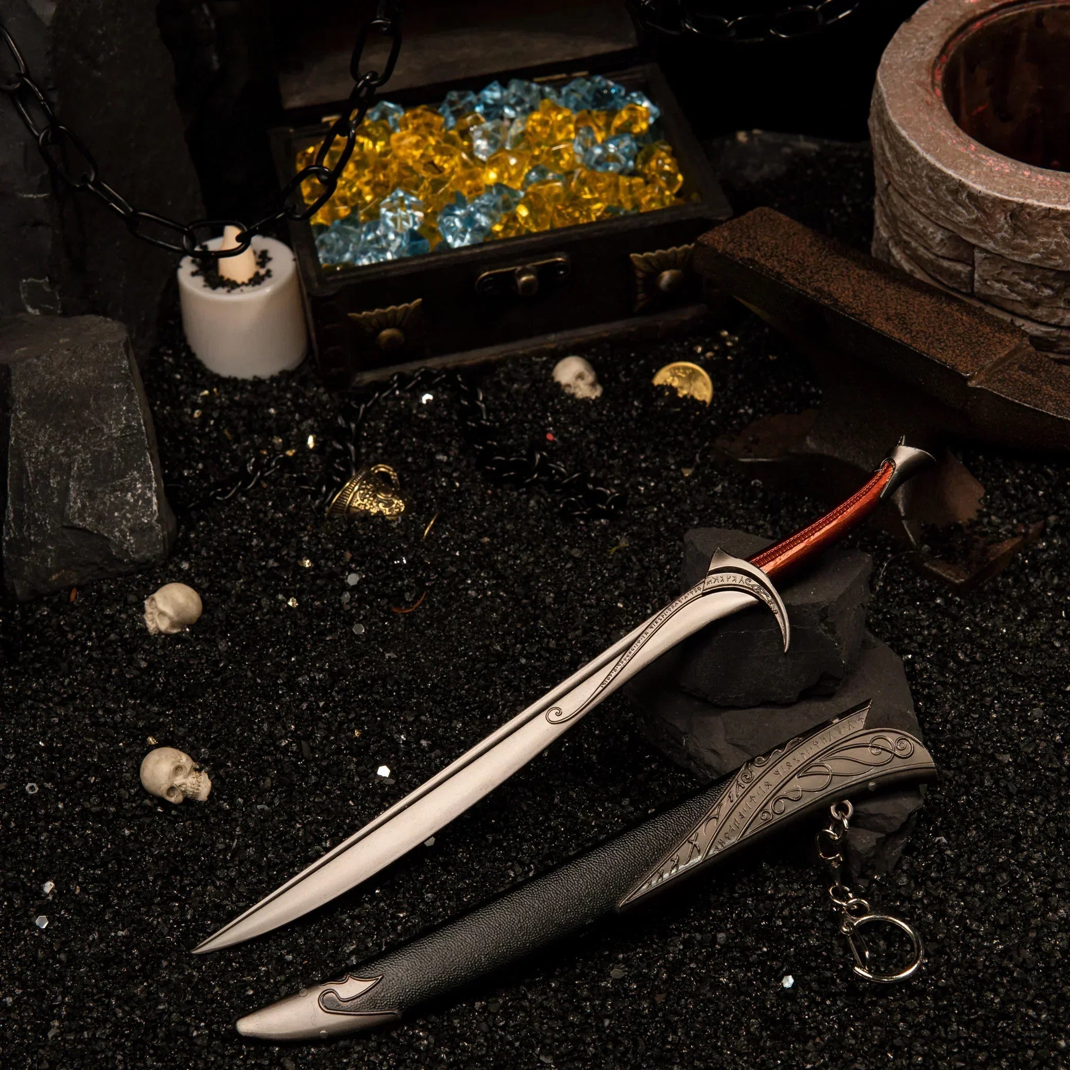 Orcrist metal replica unsheathed on black sand next to a chest of yellow and blue gems, skulls, and a black anvil.