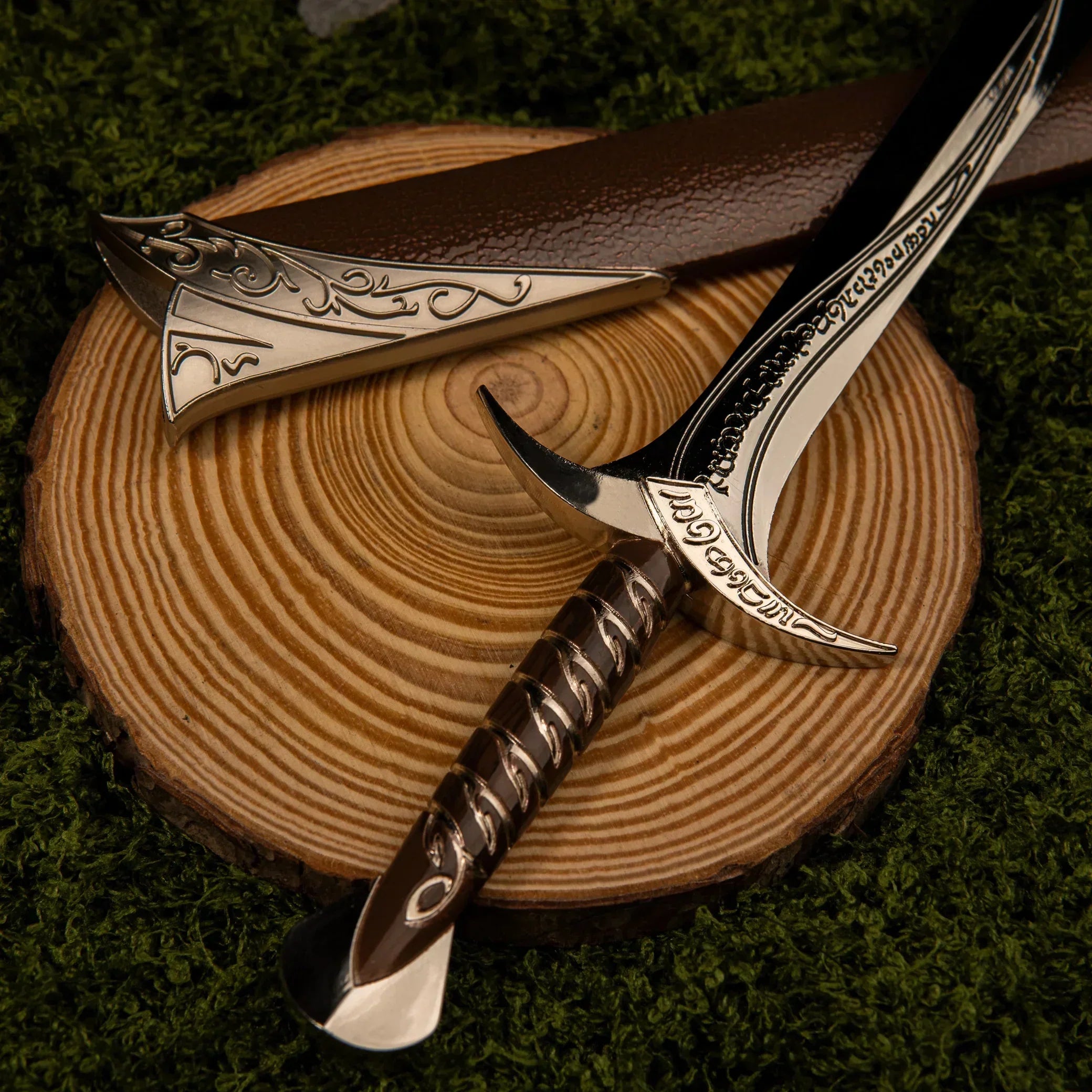 Macro close-up of the Sting replica sword's hilt resting on a wooden slice, showing Elven leaf engravings.