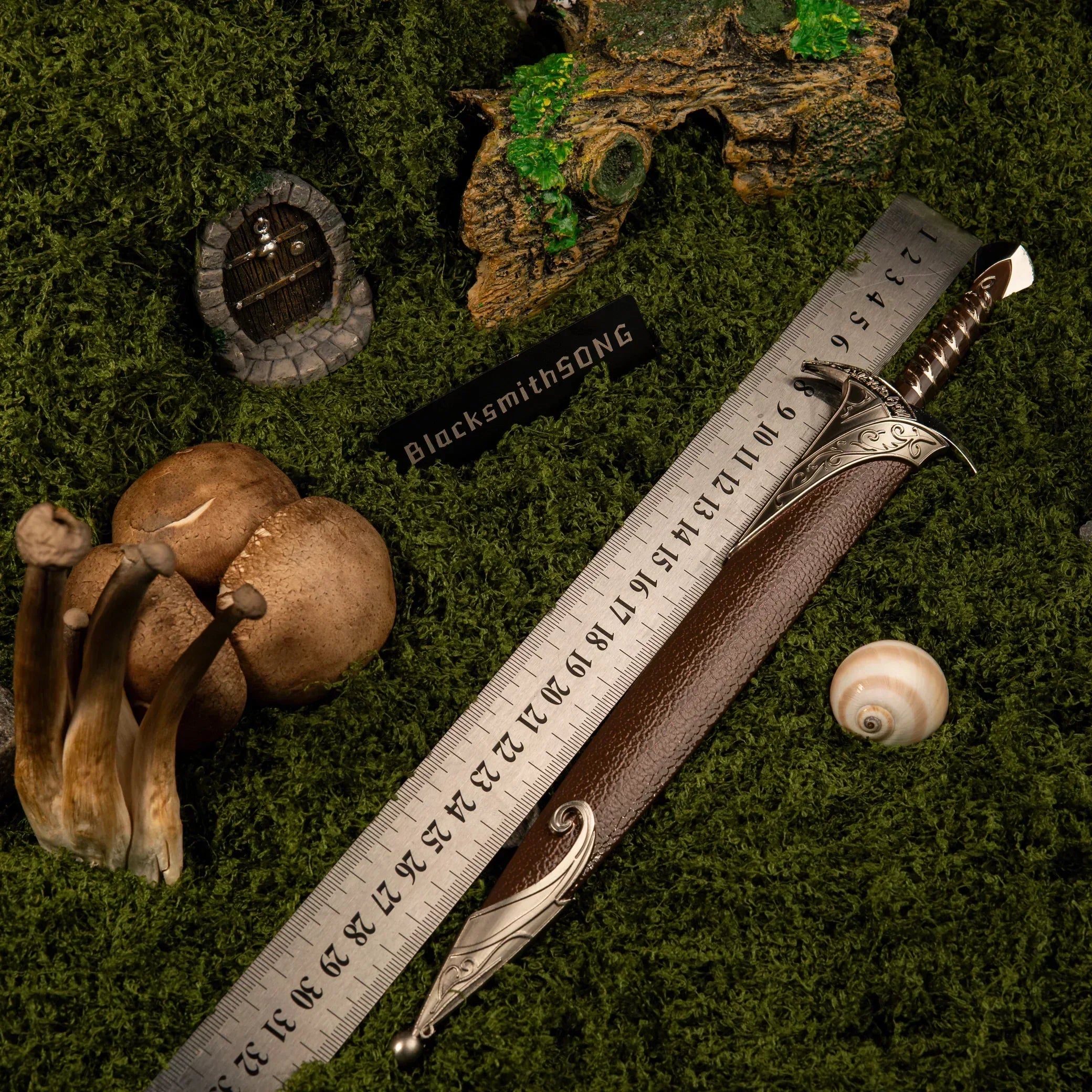 Metal ruler measuring the sheathed Sting replica, confirming its 30cm length on the green moss.