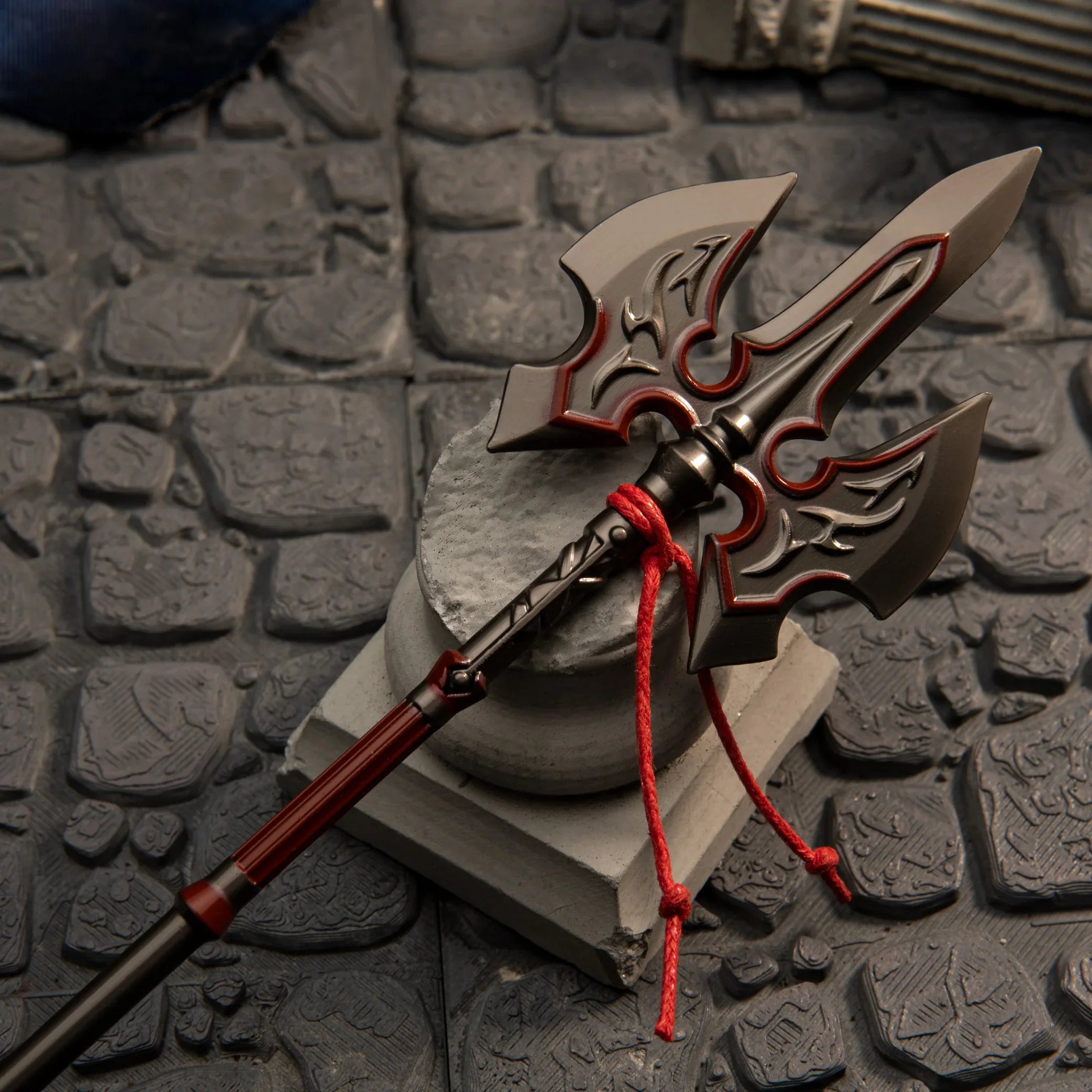 Close-up of the Royal Guard's Spear metal miniature resting on a broken white pillar, highlighting the crimson red painted details.