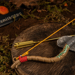 Detailed view of the metal Zelda Wooden Bow tip, showing the bright red cord binding and the taut elastic string holding the golden arrow against a mossy background.