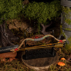The Zelda Wooden Bow miniature displayed horizontally on a large black rack with the golden arrow resting below, set in front of a stone watchtower diorama.