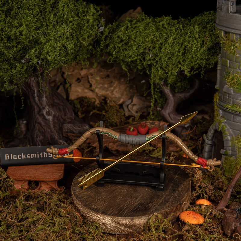 The metal Zelda Wooden Bow replica resting symmetrically on a compact black desk stand, with the golden arrow lying across the base amidst moss and mushrooms.