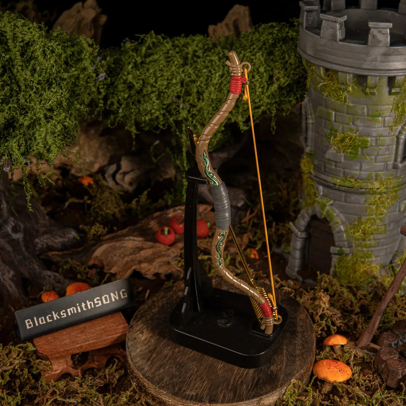 An upright vertical display of the 18cm metal Zelda Wooden Bow and golden arrow on a black base, standing tall in a miniature Hyrule camp setting.